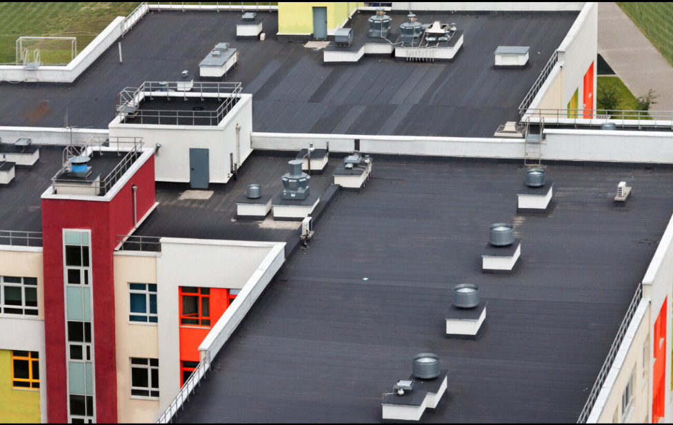 Comprehensive Overview of Commercial Roofing in Canton 1 Aerial view of a flat industrial roof with multiple air vents and AC units, adjacent to a building with colorful facades.
