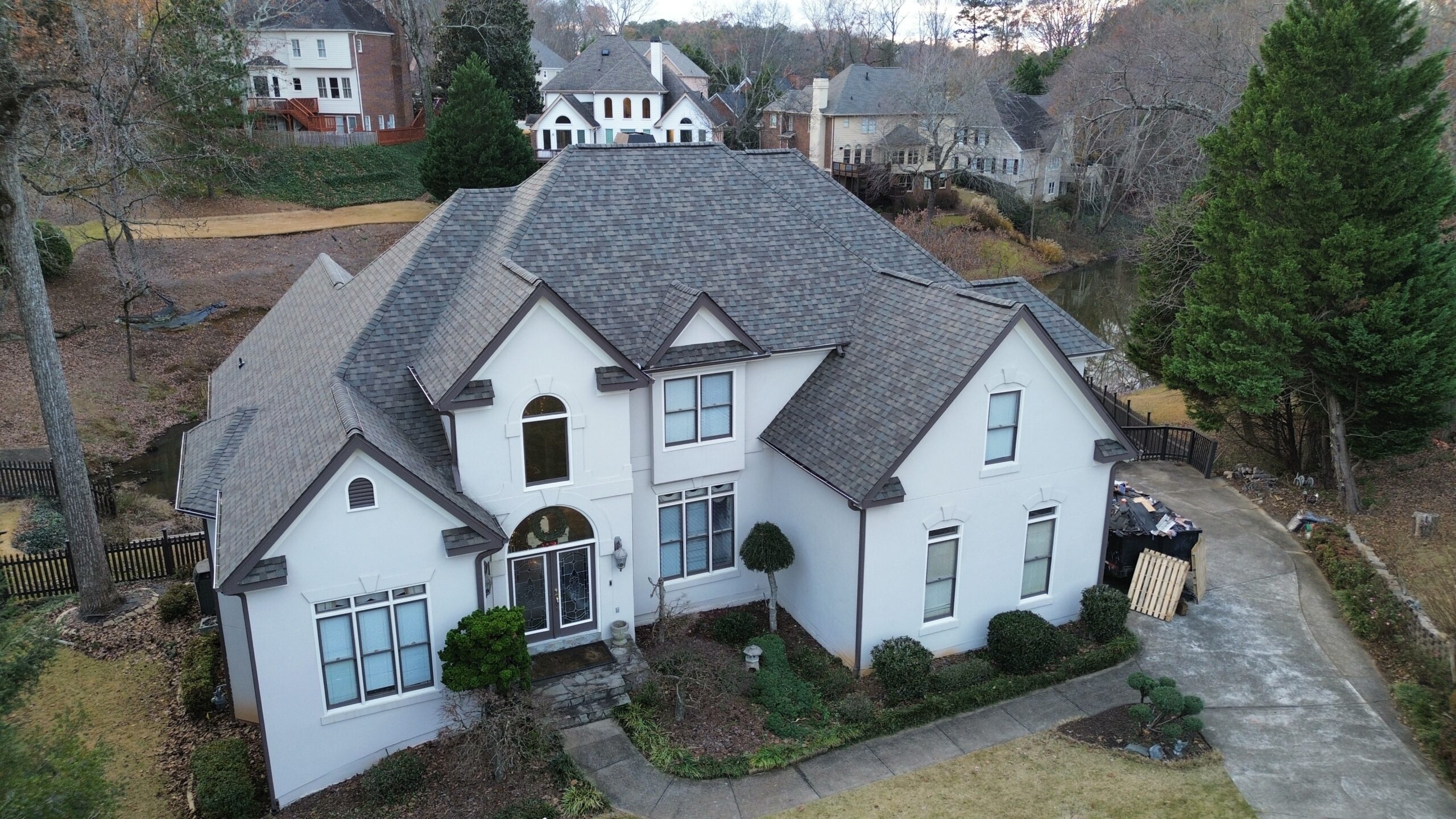 Aerial view of a two-story white house with a gray shingle roof and arched entryway, surrounded by trees and neighboring homes.